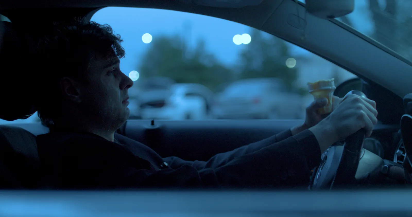 A man drives at blue hour with an ice cream cone in one hand